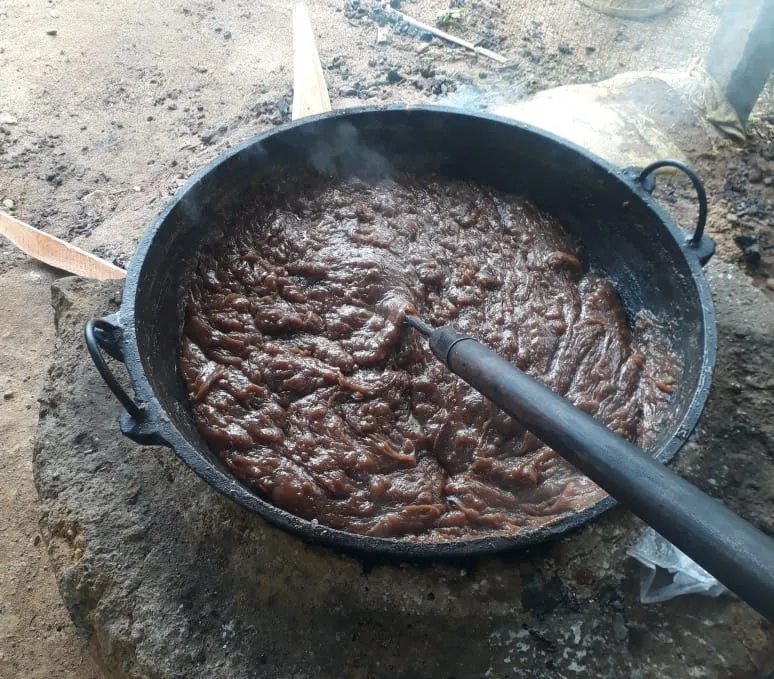A large pan of dark mixture cooking over a wood fire